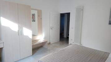 A bedroom with a bed, a wardrobe, a radiator, and a door leading to another room.