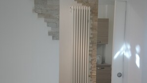 Un pasillo con piso de baldosas, un radiador y una puerta que da a una zona de cocina.