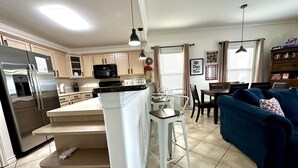 Una cocina moderna con una isla central, un área de comedor con un sofá azul y una sala de estar con televisor.