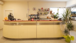 A hotel reception area with a curved counter, a coffee machine, and a variety of bottles on shelves. - RistHotel Airport (Fogliano Redipuglia)
