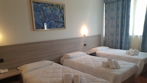 A hotel room with three beds, each with a quilted white duvet and rolled towels. There is a painting on the wall above the beds, a bedside lamp, and a window with curtains. - RistHotel Airport (Fogliano Redipuglia)