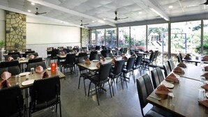 A spacious indoor dining area with multiple tables and chairs, ceiling fans, and large windows providing natural light. - Basilica Holiday Home (Mawal)
