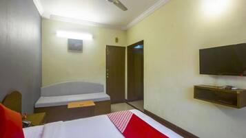 A hotel room with a bed, a desk, a chair, a television, and a ceiling fan.