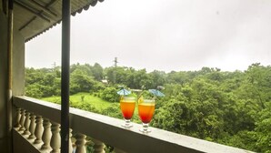 A balcony with two glasses of drink and a view of a lush green landscape. - Basilica Holiday Home (Mawal)