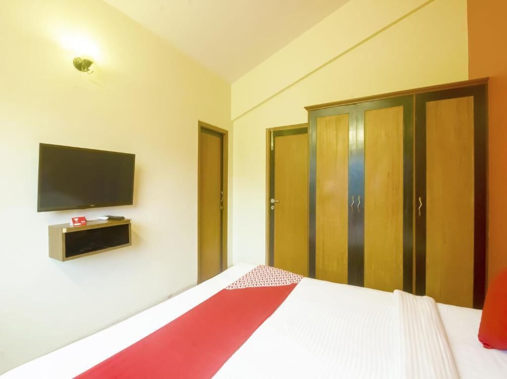 A hotel room with a bed, a TV mounted on the wall, and a wardrobe with two doors.