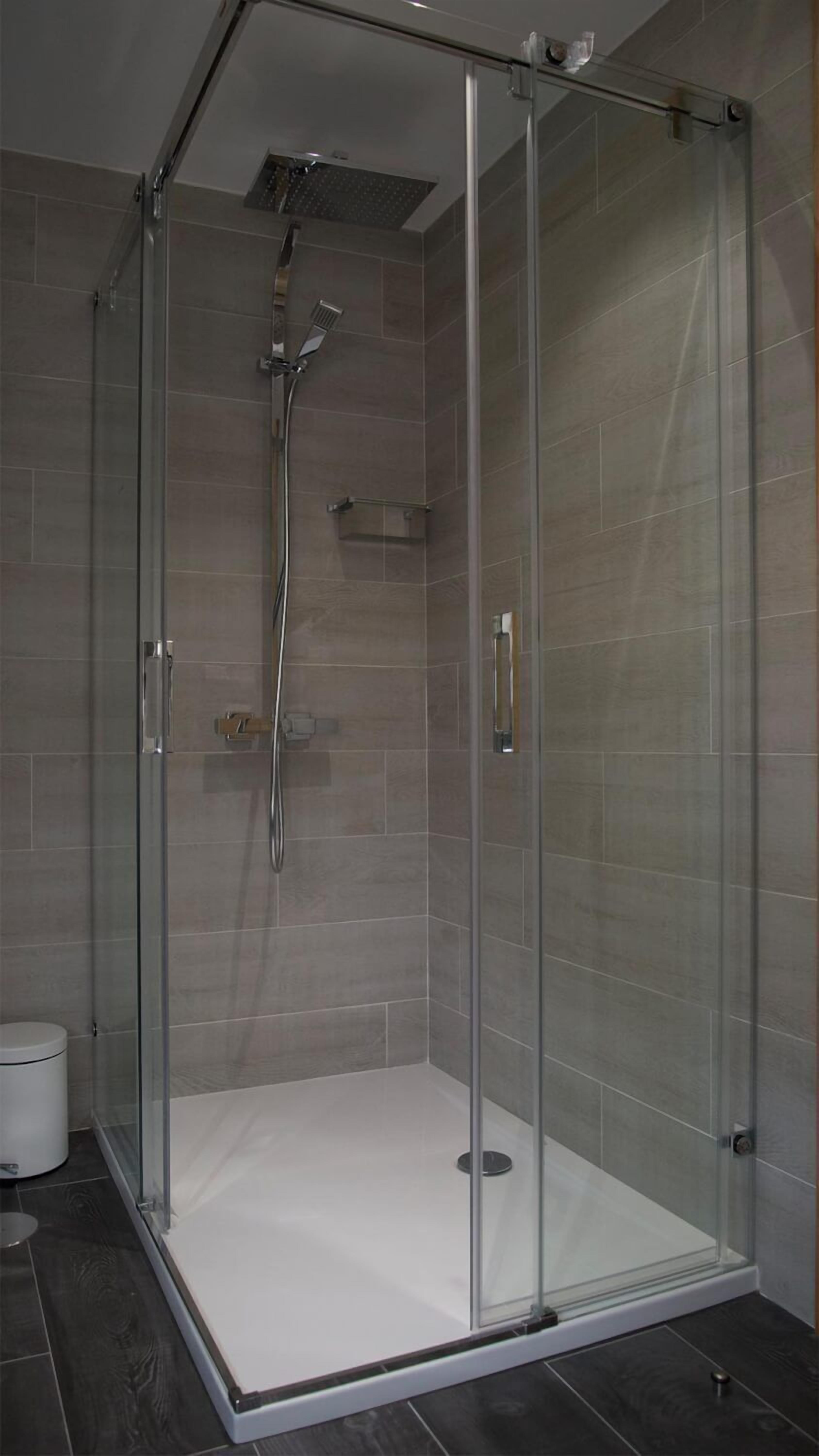 Cabina de ducha con paredes de vidrio, un cabezal de ducha de mano y un grifo instalado en la pared.