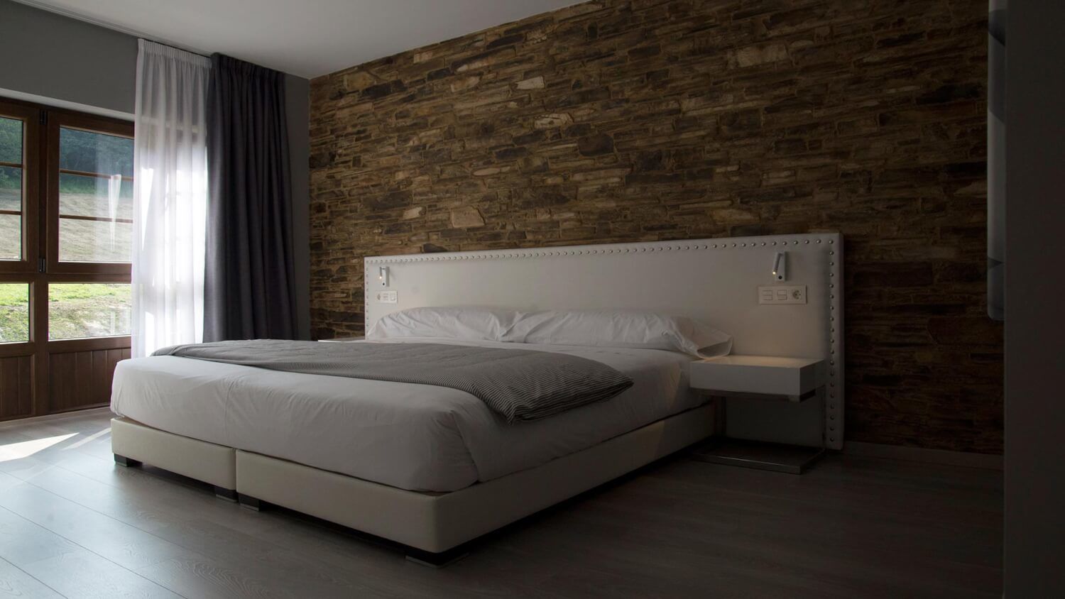 A modern bedroom with a large bed, a wooden accent wall, and a nightstand.