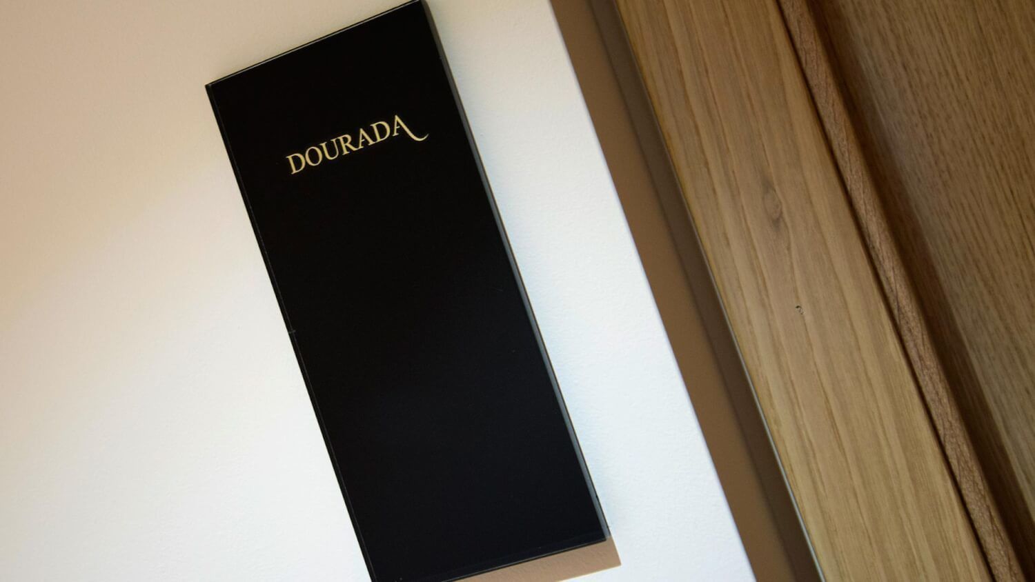 A black box with the word "DOURADA" on it, placed on a white surface next to a wooden table.