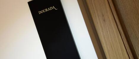 A black box with the word "DOURADA" on it, placed on a white surface next to a wooden table.