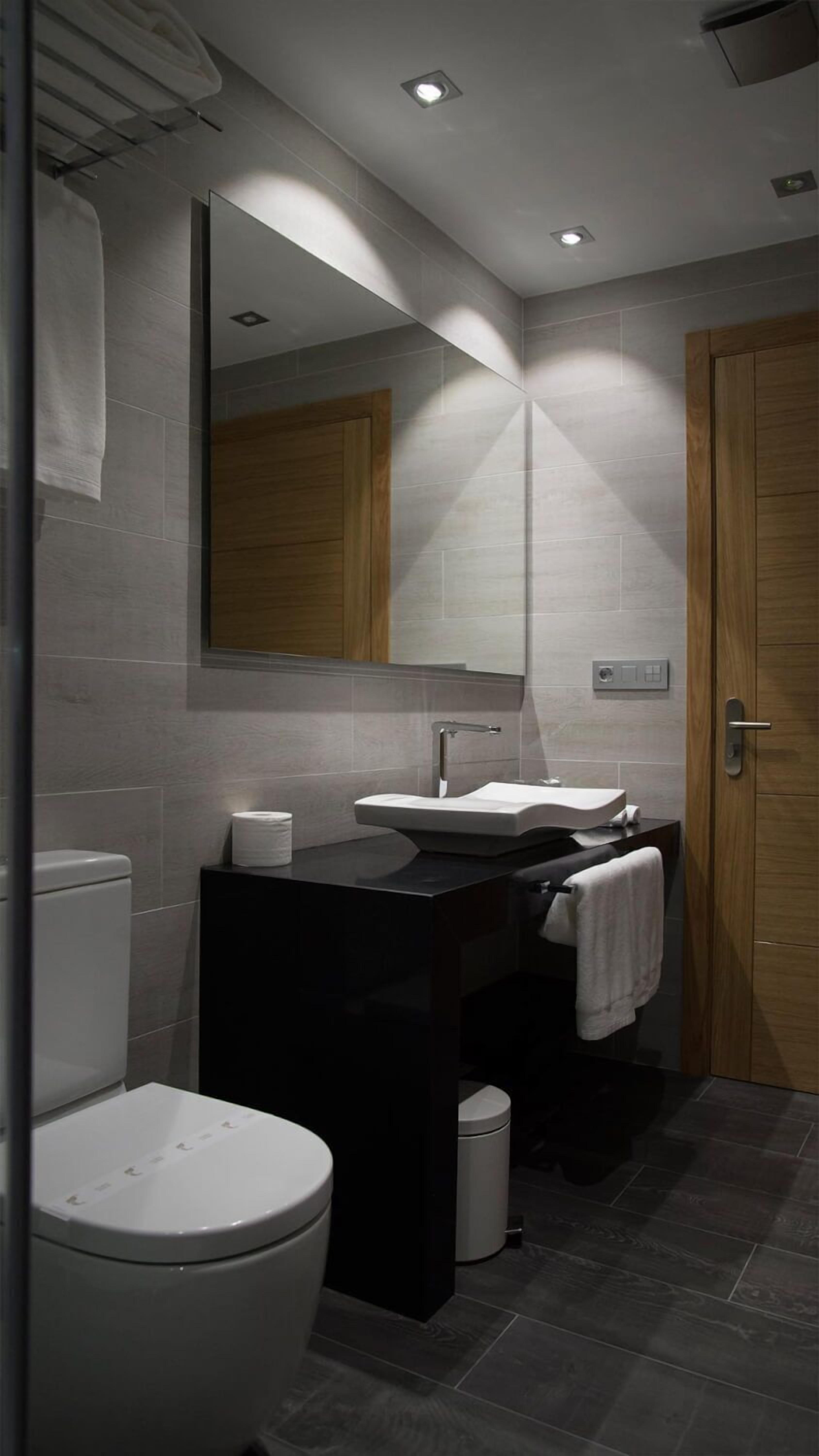 Un baño moderno con un inodoro blanco, un lavabo negro y un espejo encima.
