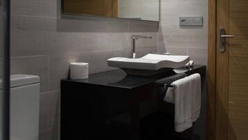 Un baño moderno con un inodoro blanco, un lavabo negro y un espejo encima.