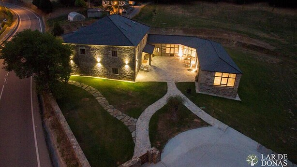 A stone house with a curved roof, a well-lit driveway, and a surrounding lawn. - Lar de Donas (Meira)