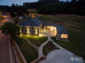 A stone house with a curved roof, a well-lit driveway, and a surrounding lawn. - Lar de Donas (Meira)