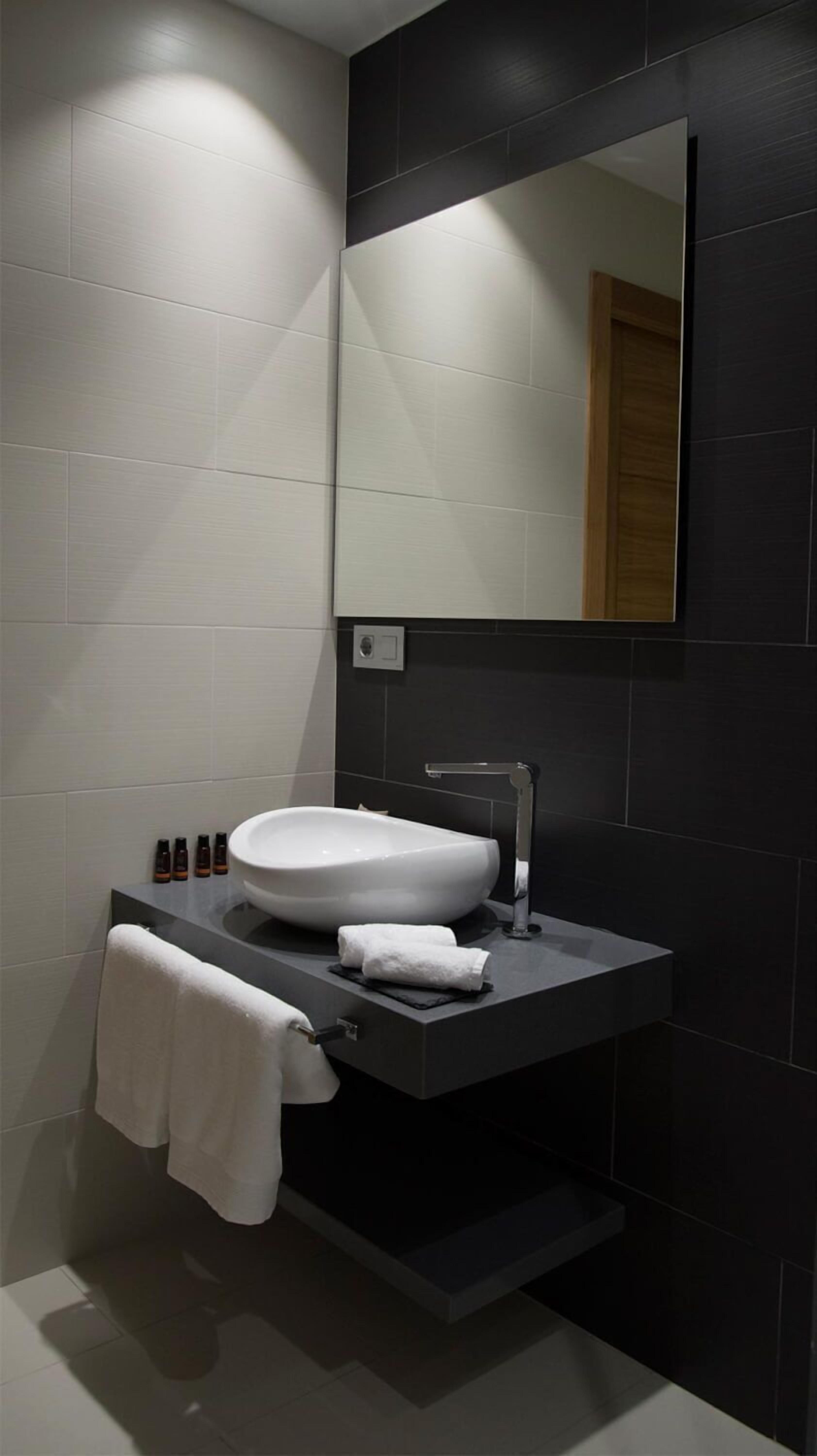 A modern bathroom with a white sink, dark tiles, and a mirror.