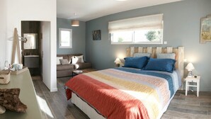 A bedroom with a large bed, a bedside table, a nightstand, a window with blinds, a mirror, and a door leading to another room.