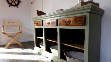 Un mobile verde con tre cassetti e due ripiani, una sedia di legno con un cartello e una ruota di timone appesa al muro.