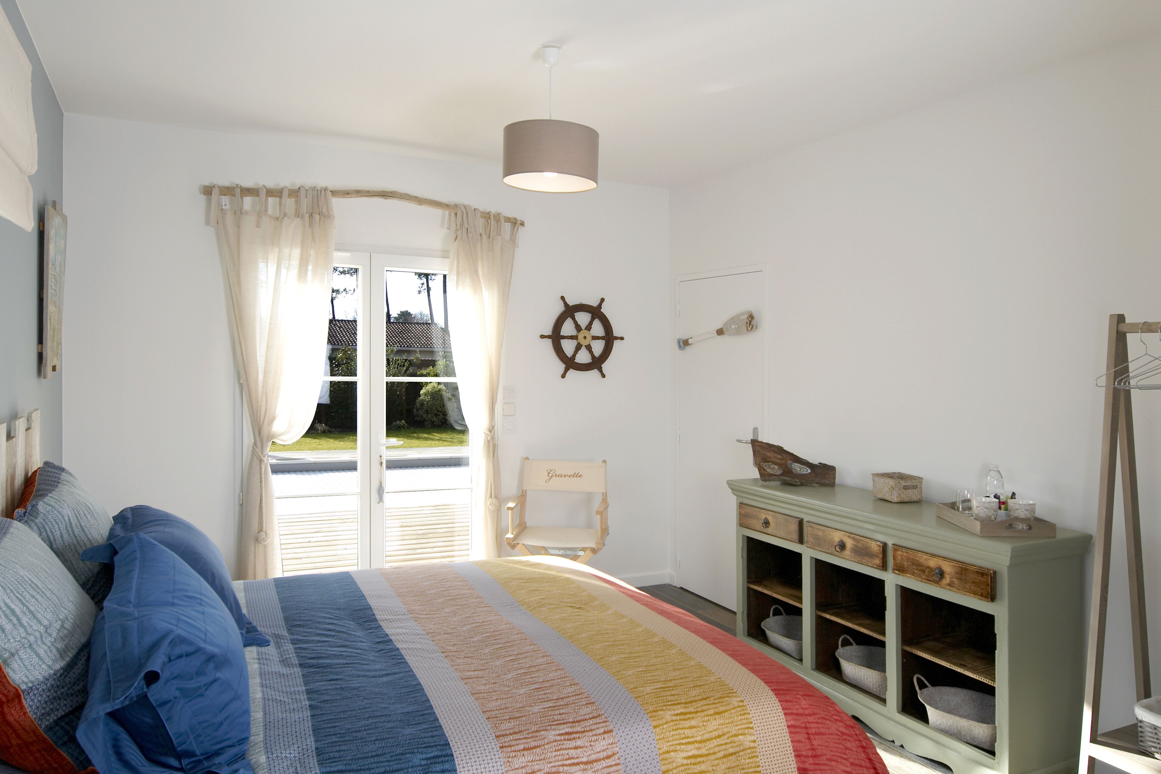 Een slaapkamer met een groot bed, een houten stoel, een dressoir en uitzicht op het landschap.