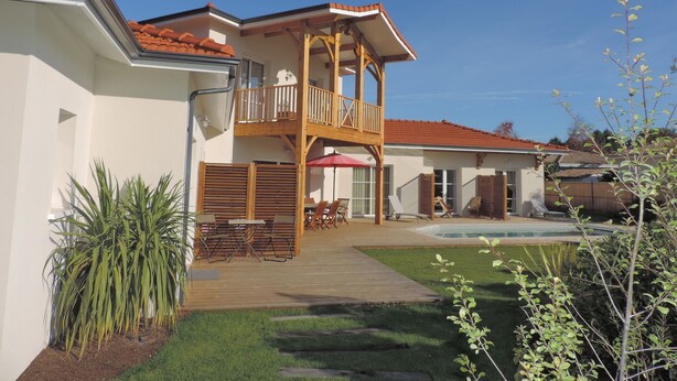 A two-story house with a wooden balcony, a swimming pool, and a garden area.