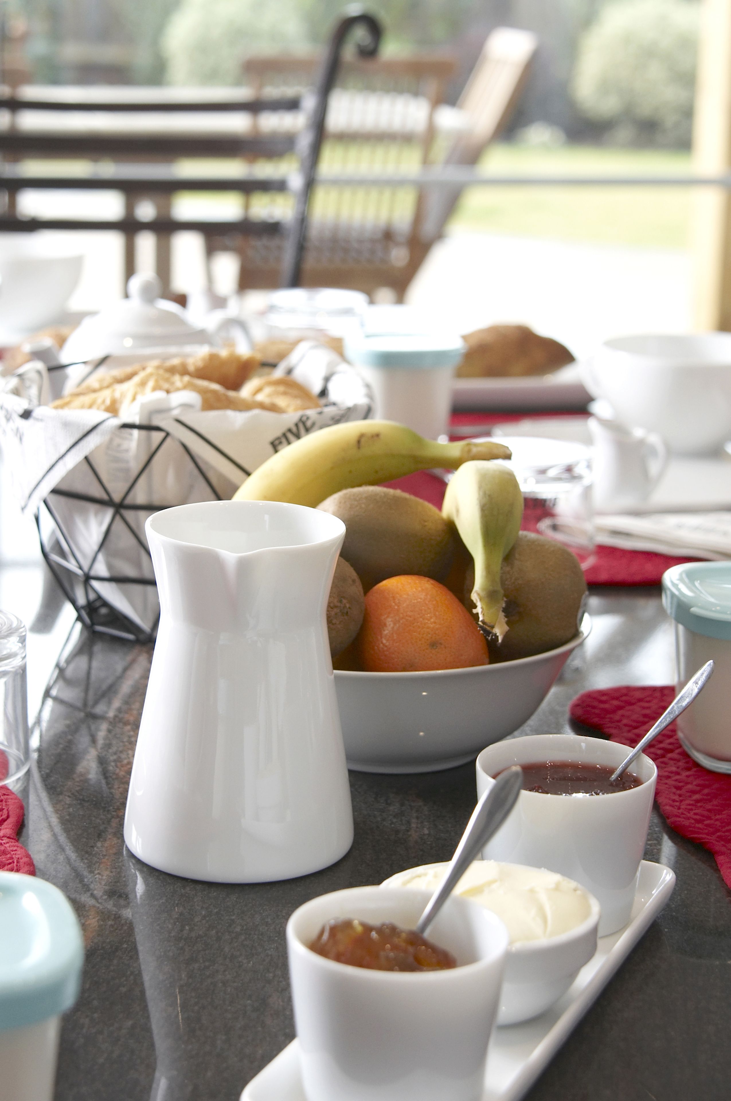 A breakfast table with a fruit bowl, a pitcher, and small bowls of jam and cream.
