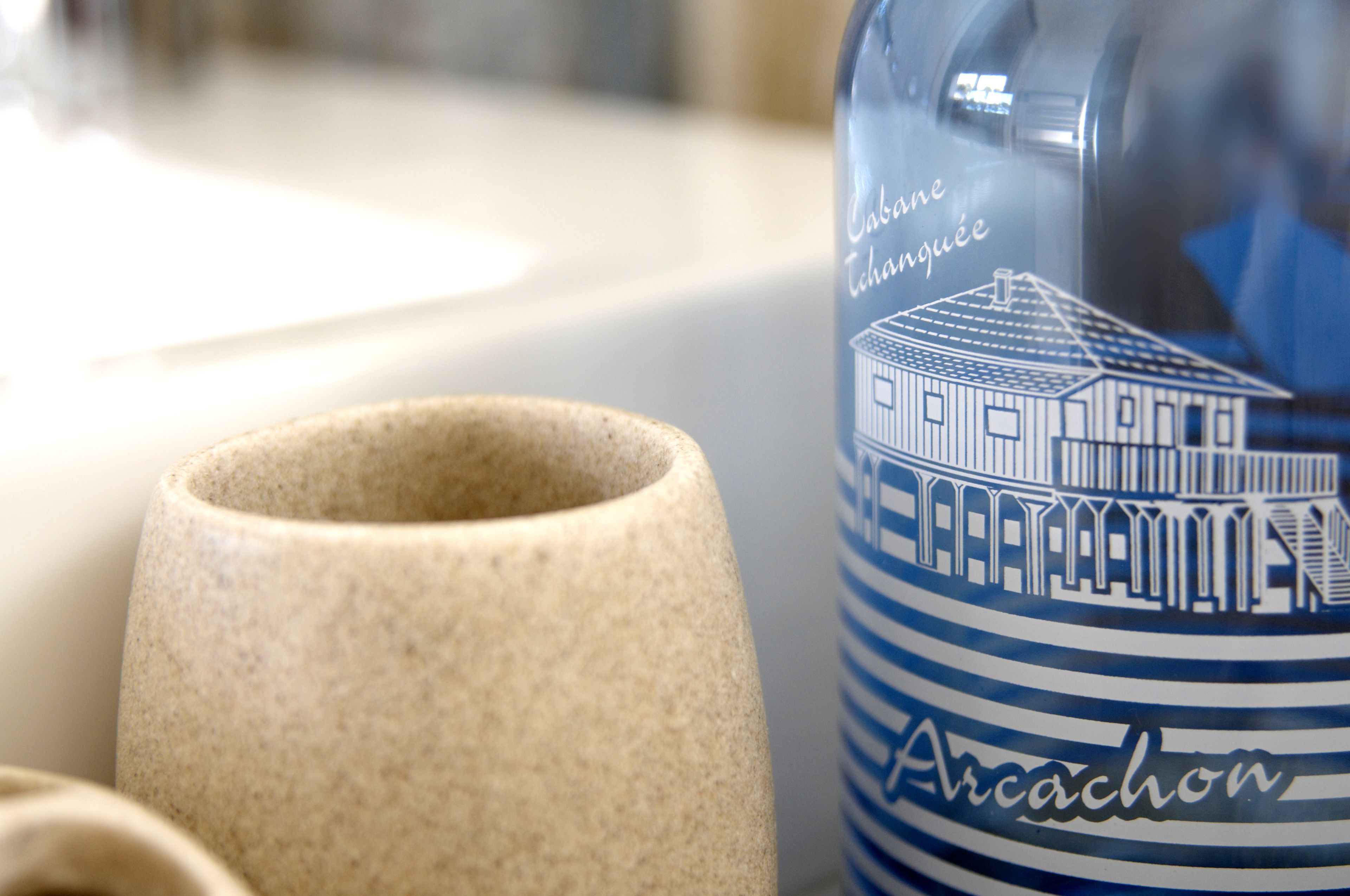 Eine Keramiktasse und eine Flasche mit einer Illustration eines Gebäudes und dem Schriftzug 'Arcachon'.