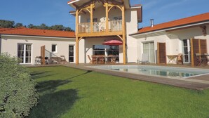 A two-story house with a wooden balcony, a swimming pool, and a well-maintained lawn.