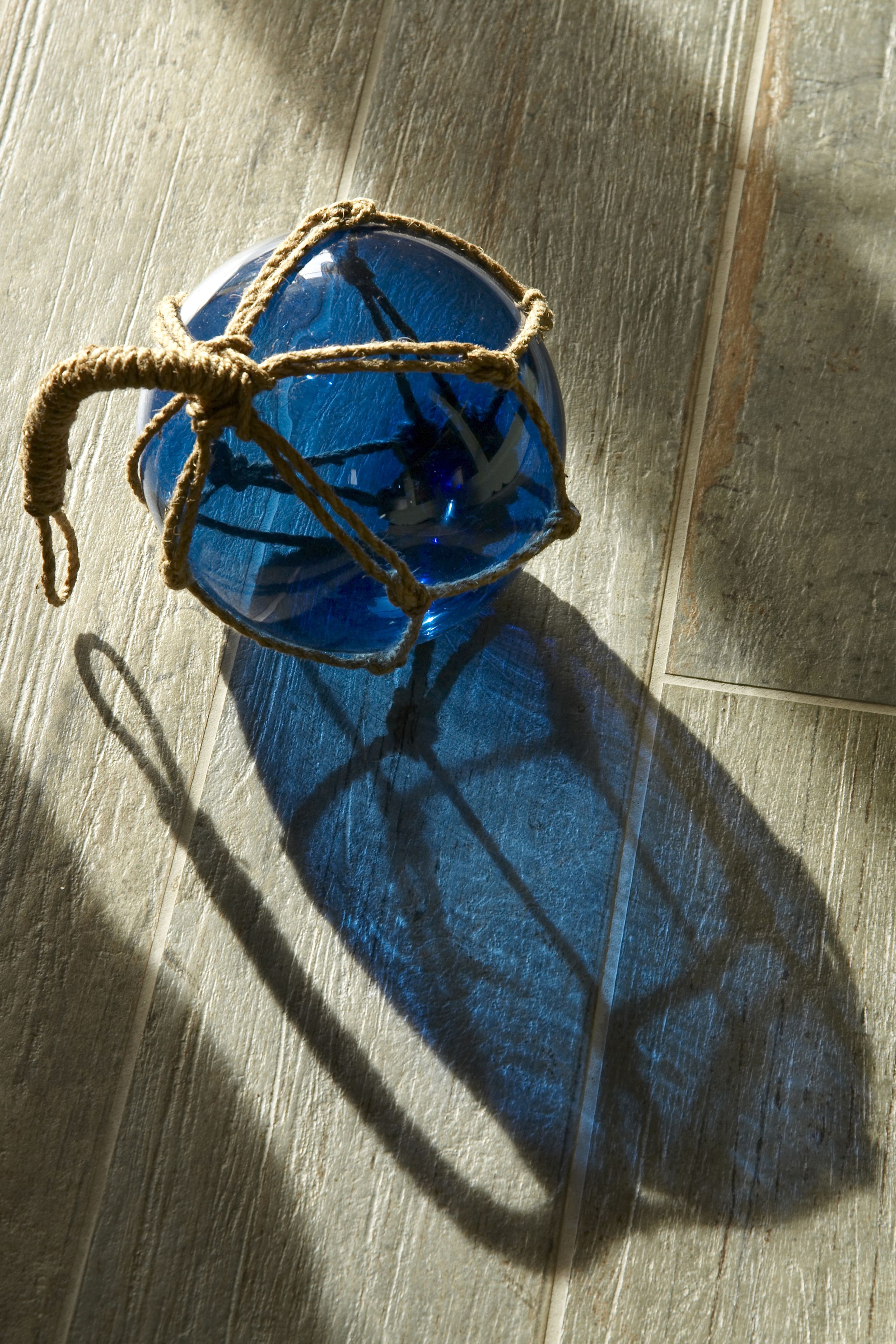 A blue glass object with rope tied around it, placed on a wooden floor.