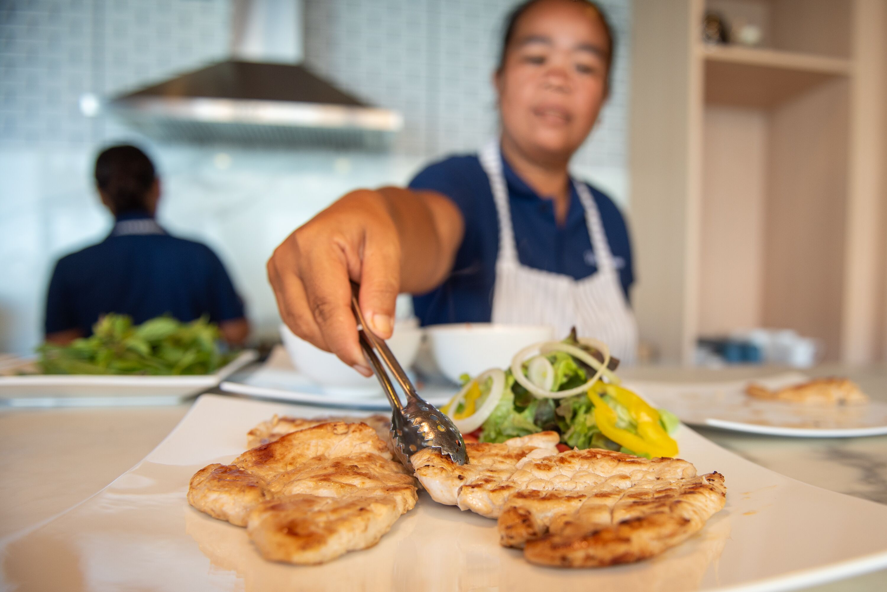 A person serving grilled chicken on a plate with a side salad.