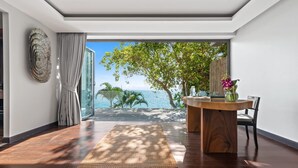 A modern room with a large window overlooking a tropical beach, a wooden desk, and a woven rug.
