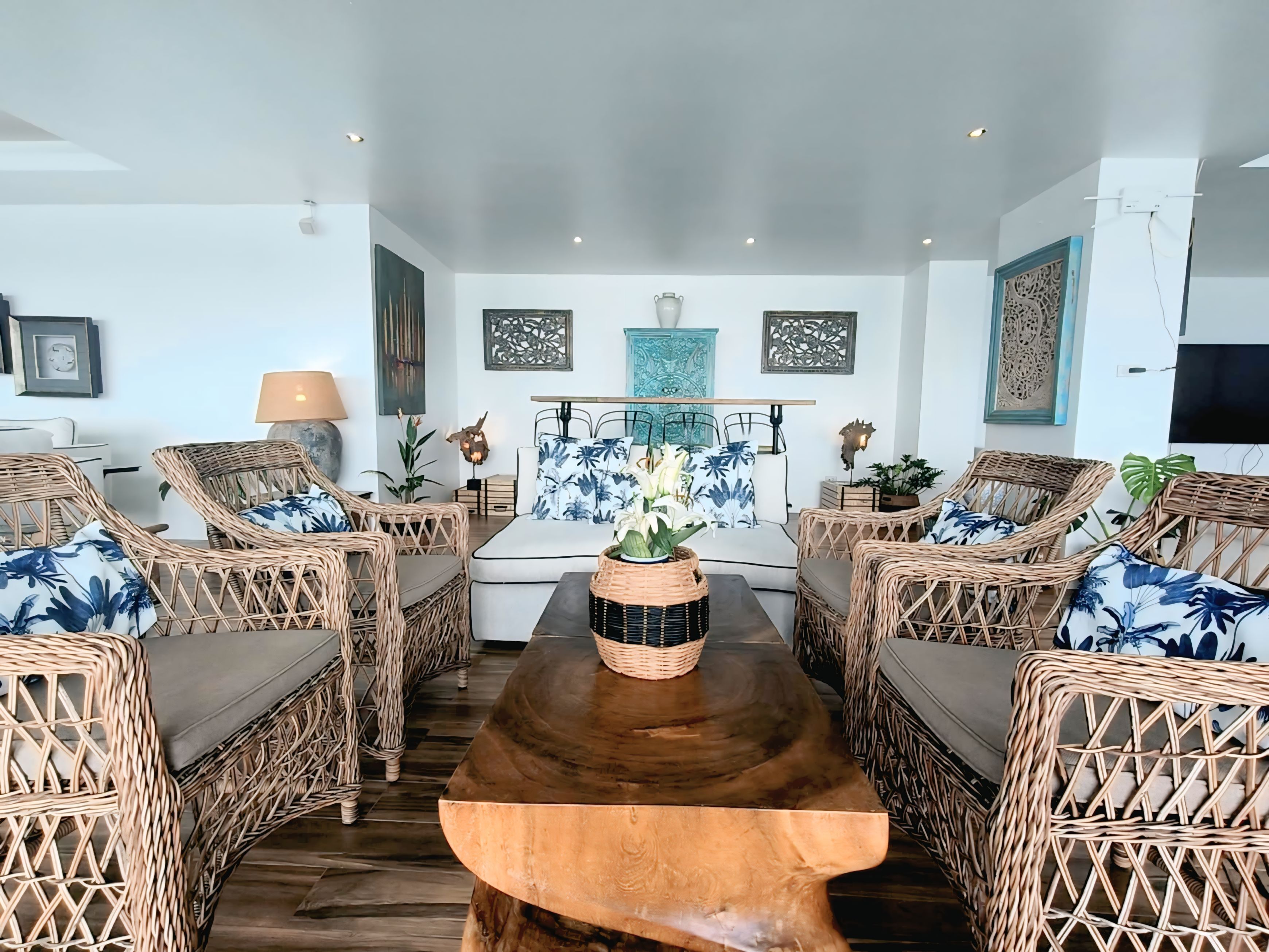 Un salon avec des meubles en osier, une table basse en bois et des œuvres d’art décoratives accrochées au mur.