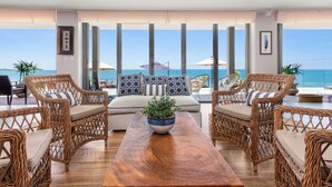 A spacious living area with wicker furniture, a wooden coffee table, and a view of the ocean.