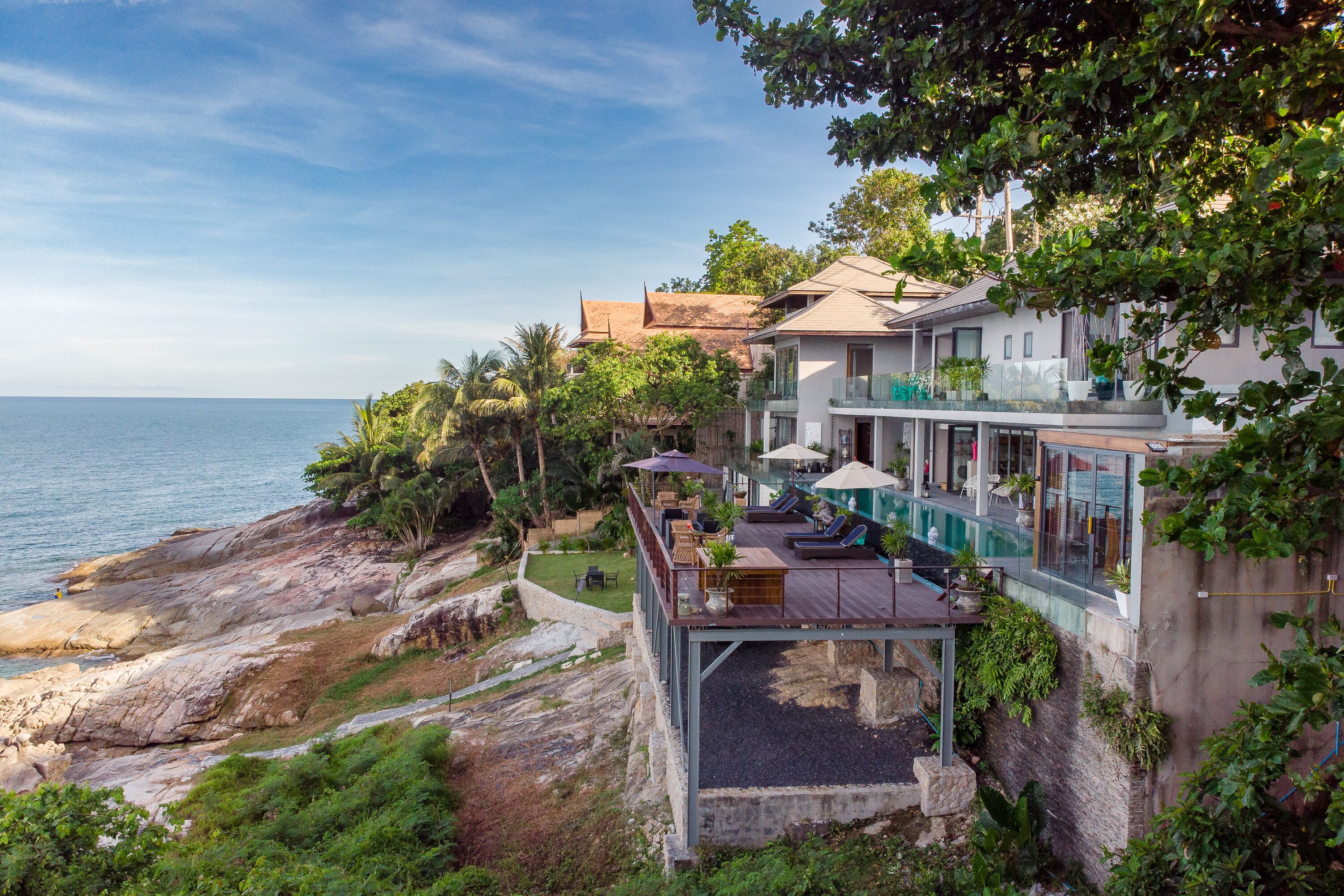 A coastal property with a pool, outdoor seating, and a view of the sea.
