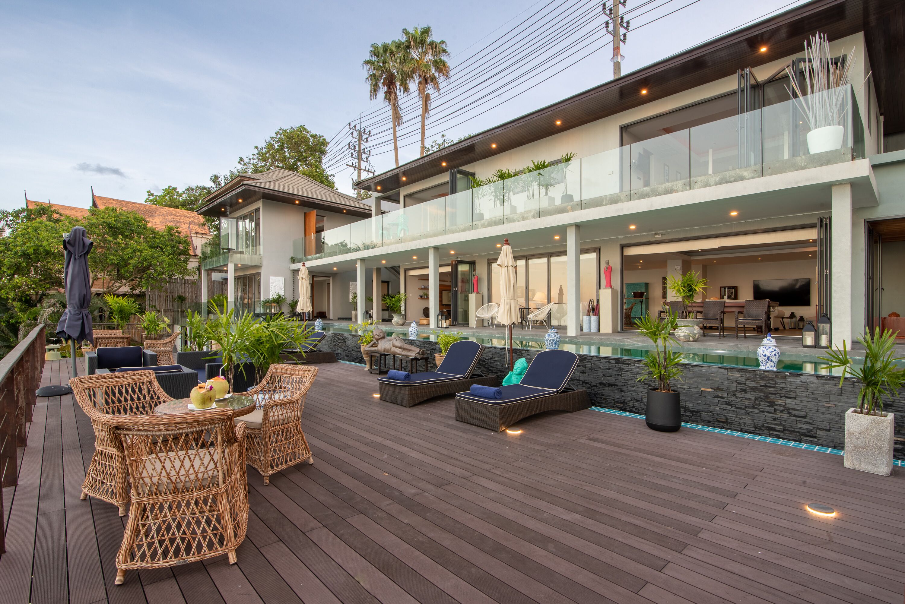 Una terraza moderna al aire libre con mobiliario de mimbre, piscina y zona de estar cubierta con vidrio.