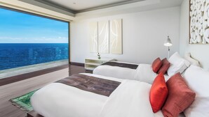 A modern hotel room with two beds, a large window with a view of the ocean, abstract wall art, and a small side table with a vase.