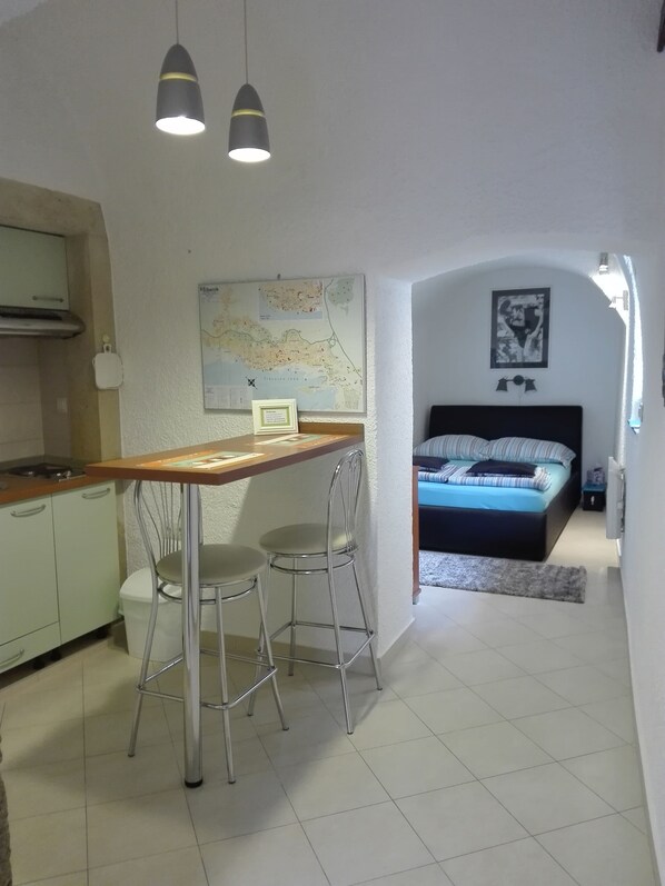 A compact living space with a kitchenette, a dining area with a table and chairs, a bed with a blue mattress, and a map on the wall.