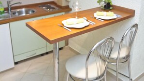 A small kitchen with a wooden table and two metal chairs, a sink, and a stove. - Apartment Toma (Sibenik)