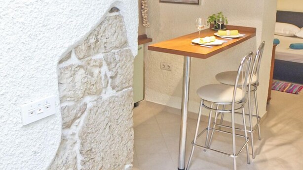 A dining area with a stone wall, a wooden table, two chairs, and pendant lights. - Apartment Toma (Sibenik)