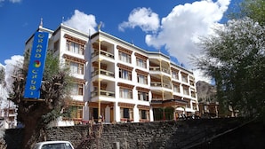 Un hotel de varios pisos con balcones, un muro de piedra y un coche estacionado al frente.