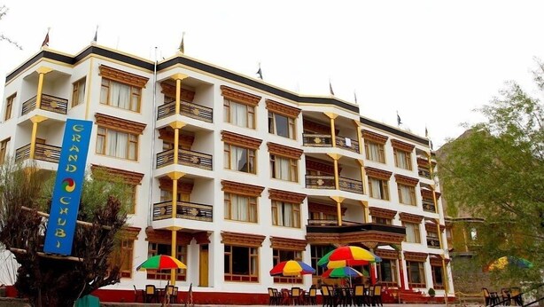 Un hotel de varios pisos con balcones, mesas al aire libre y un cartel llamativo.
