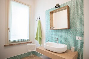 A bathroom with a window, a sink, a mirror, and a green towel hanging on hooks. - Azienda Agricola Le Colombare (Nogarole Rocca)