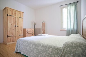A bedroom with a bed, a wooden wardrobe, a dresser, and a window with curtains. - Azienda Agricola Le Colombare (Nogarole Rocca)