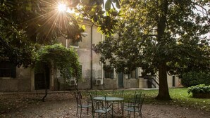An outdoor seating area with a table and chairs, surrounded by trees and a building in the background. - Azienda Agricola Le Colombare (Nogarole Rocca)