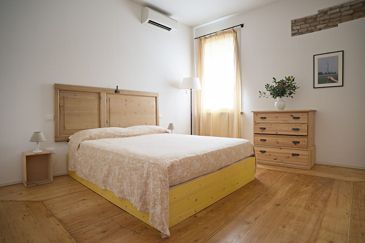 Un dormitorio con una cama de madera, una mesita de noche, un aparador y una ventana con cortinas.