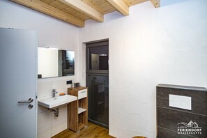 Un baño moderno con tocador de madera, un lavamanos blanco y un espejo grande.
