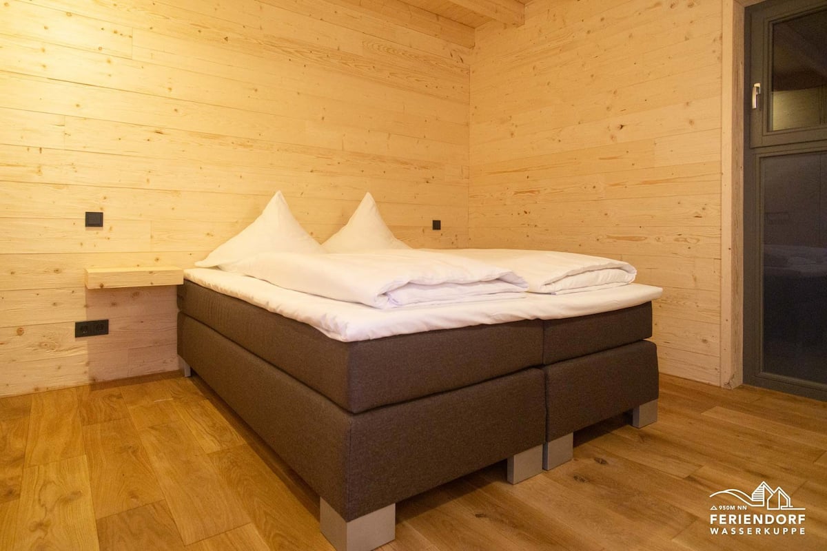 A wooden cabin room with a bed, a nightstand, and a door.