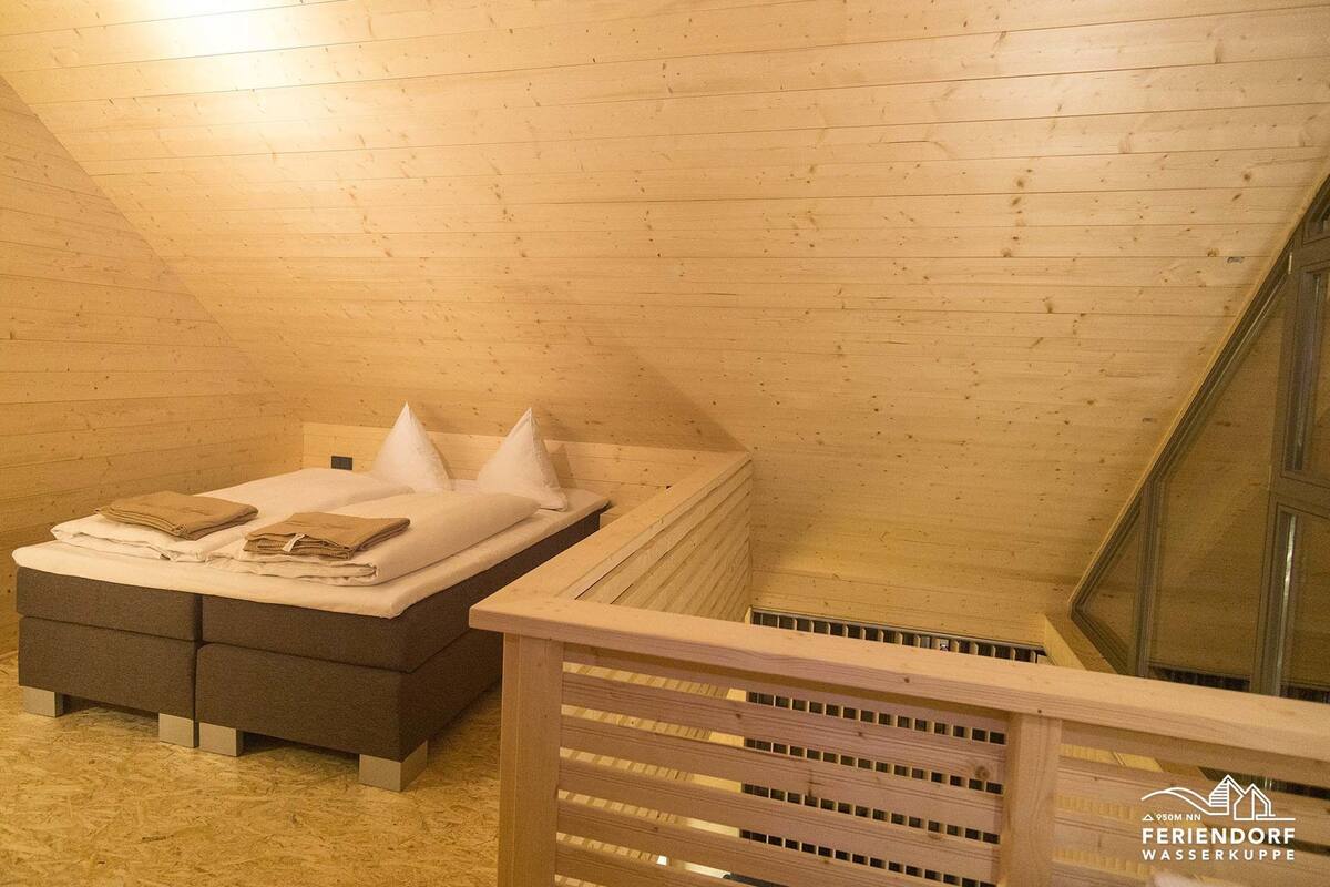 A wooden room with a bed, a bench, and a window.