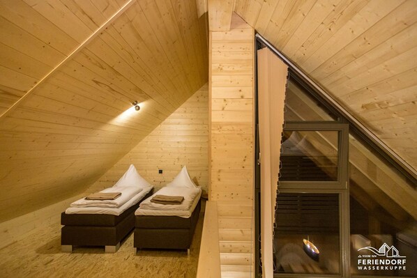 Un interior de madera con dos camas, techo inclinado y ventana visible.