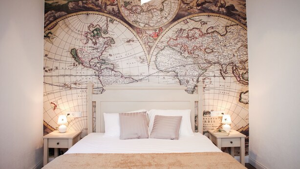 A bedroom with a large world map on the wall, a bed with white bedding, and two bedside tables with lamps.