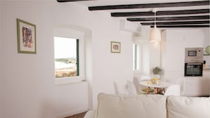 A cozy living area with a sofa, a dining table with chairs, a small kitchen with an oven, and a view of the outdoors through a window.