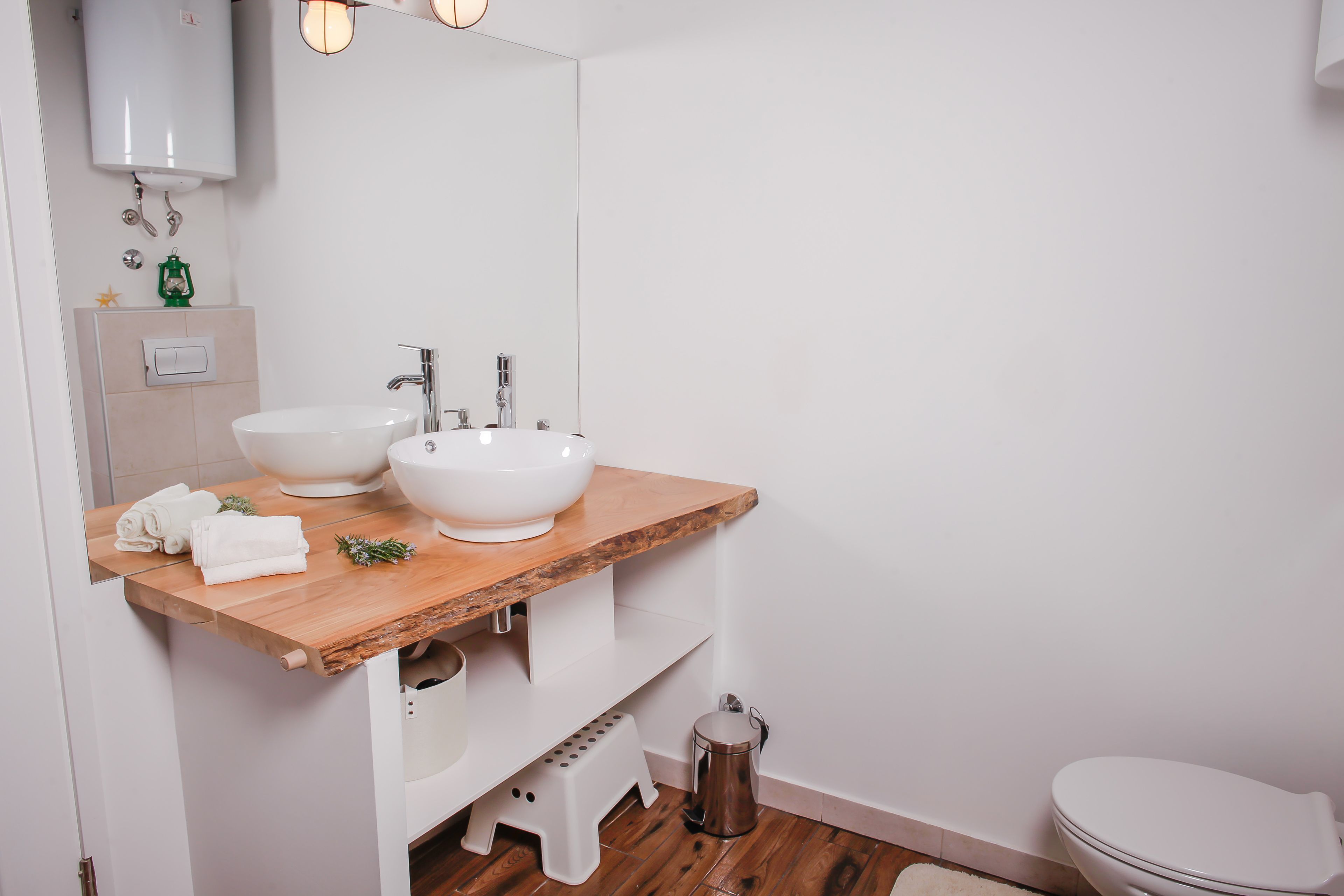 A modern bathroom with a wooden vanity, two white sinks, a mirror, and a toilet.