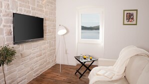 A room with a stone wall, a mounted TV, a window with a view of a lake, a small table with glasses and lemons, and a white sofa.